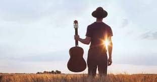 A man that plays country music with a hat and a guitar starring in the sunset